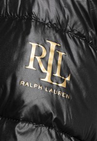 Svart glänsande tyg med sydda sömmar och guldiga Ralph Lauren-logotypinitialer "RLL" samt tryckt text på det.