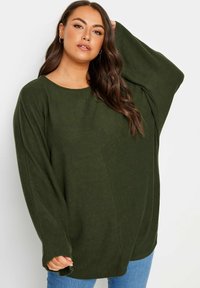 Långärmad, oversized topp i mörkgrön, tillverkad av mjukt material. Har en rund halsringning och avslappnad passform, med sänkta axlar.