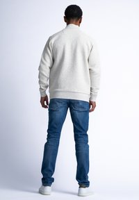 Ljusgrå texturerad sweatshirt med hög krage, kombinerad med mörkblå jeans och vita sneakers, sedd bakifrån.
