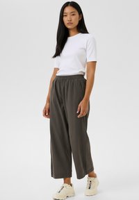 Balti trumpomis rankovėmis marškinėliai, derinami su laisvomis, tamsiai pilkomis plačių kojų kelnėmis. Modelis dėvi šviesios spalvos sportinius batelius. Paprasta, kasdieninė apranga.