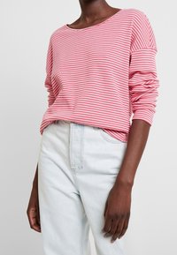 Rød og hvid stribet langærmet top lavet af blødt stof, med en oversized pasform og en bred udskæring. Parret med lyseblå jeans.