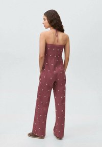 Burgundy jumpsuit with a smocked bodice, strap design, and white polka dots, featuring wide-leg trousers and soft textured fabric.