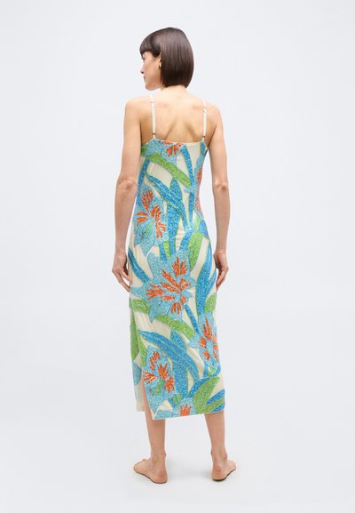 Γυναίκα με κοντά σκούρα μαλλιά που φοράει αμάνικο μίντι φόρεμα με μπλε, πράσινο και πορτοκαλί λουλουδάτο σχέδιο, όρθια ξυπόλυτη με την πλάτη προς τα εμπρός.