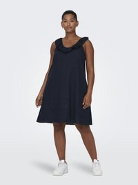 Robe sans manches bleu marine avec un col froncé, arborant un design fluide et des détails brodés au niveau de l'ourlet. Associée à des baskets blanches.