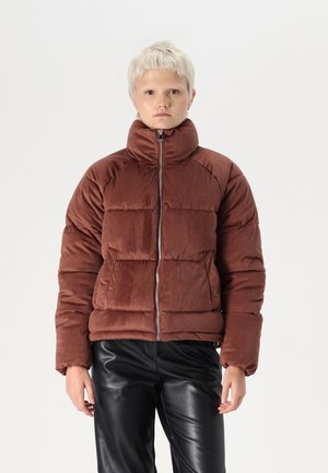 Brun fløyelsjakke med høy krage, glidelås foran og quiltet design. Kombinert med sorte skinnbukser.