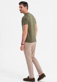 Olivově zelené tričko s krátkým rukávem, světle hnědé slim-fit kalhoty a tmavě hnědé boty, z pohledu zezadu, se zaměřením na volný střih a barvy.