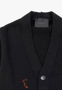 Zwarte gebreide cardigan met een V-hals ontwerp, voorzien van een sluiting met knopen aan de voorkant en een geborduurd detail in oranje aan de linkerzijde.