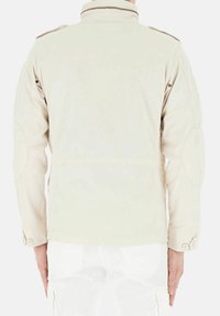 Giacca in cotone beige con colletto a pistagna, polsini con bottoni e toppe sui gomiti. Presenta una chiusura con zip e dettagli sui fianchi.