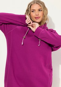 Sweatshirt à capuche violet en tissu doux, doté d'une poche kangourou à l'avant, de cordons de serrage aux couleurs contrastées et de poignets côtelés.