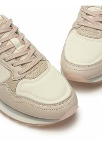 Beige sneakers met een mix van leer en stof, een ronde neus, textuuraccenten en platte veters over een zachte tong.