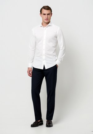 Witte blouse met lange mouwen en knopen, met een gladde textuur, gecombineerd met marineblauwe broek en zwarte schoenen, voorzien van een klassieke pasvorm en subtiele details.