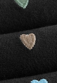 Tela negra con bordados texturizados que presenta tres corazones: verde, marrón y azul claro, dispuestos en un patrón repetitivo.