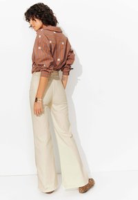 Chemise rayée brune avec broderie florale blanche, associée à un pantalon large taille haute crème et des chaussures à imprimé animal.