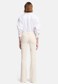 Witte blouse met opgestoken mouwen, gecombineerd met lichtbeige uitlopende jeans met achterzakken en een gladde textuur.
