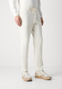 White relaxed-fit pants with a drawstring waistband, paired with light beige and gray sneakers, featuring a textured surface and running sole.