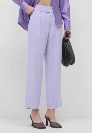 Person wearing light purple wide-leg trousers, a satin lavender shirt, black mesh high-heeled shoes, holding a black slouchy clutch bag.