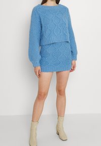 Ljusblå stickad tröja och kjolset med en strukturerad diamantmönster, ribbade detaljer och långa ärmar. Skorna är beige anklarboots.