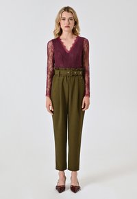 Top in pizzo bordeaux con scollatura a V profonda, abbinato a pantaloni verdi oliva a vita alta con vita cintata e gambe affusolate.