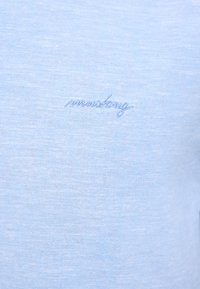 Camiseta de algodón azul claro con una textura suave y un sutil logo bordado en azul más oscuro en el lado izquierdo del pecho.