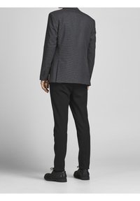 Grijs patroon blazer met gestructureerde schouders, enkele split en manchetten met drie knopen, gedragen met slim-fit zwarte broeken en veterschoenen.