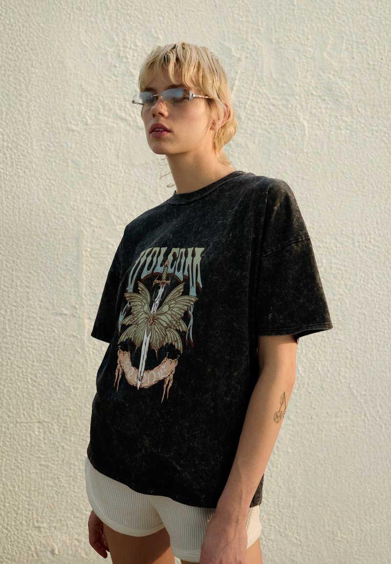 Schwarzes übergroßes T-Shirt mit einem Schmetterlingsgrafik in Grün und Beige, mit abgesenkten Schultern und einem weichen, strukturierten Stoff.