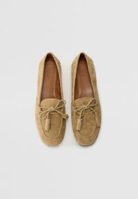 Beige semsket loafers med rund tå og dekorativ sløyfedetalj. Har frynser og en glatt lærinnersåle. Flat såle.