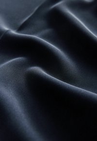 Dunkelblauer Stoff mit einer glatten, leicht glänzenden Textur, der sanfte Falten und ein dezentes geripptes Muster aufweist.