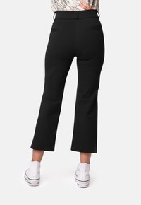 Pantalones negros acampanados con una textura suave, con una cintura alta, dos bolsillos traseros y una longitud corta. Combinados con zapatillas blancas.