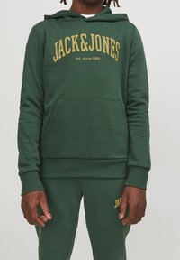 Grön hoodie med guld "JACK&JONES"-logotyp, känguruficka, ribbade muddar och nederkant, tillverkad av texturerad tyg, kombinerad med matchande gröna sweatpants.