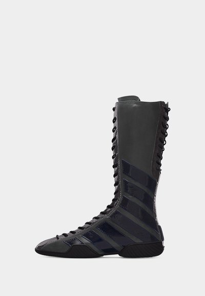 Botte de boxe haute noire à lacets avec des rayures diagonales brillantes et une semelle crantée, vue de côté sur fond blanc.