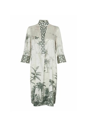 Femme portant une robe blanche longueur genou avec des motifs botaniques verts, manches trois-quarts, col mandarin et sandales noires à talons bas.
