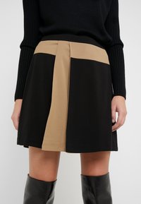 Zwart en bruin knie-lange rok met een aansluitende tailleband, voorzien van een gespleten ontwerp en een gladde textuur. Gecombineerd met een zwarte geribbelde trui.