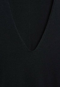 Gros plan d'un tissu tricoté noir avec un col en V et une couture visible au centre.