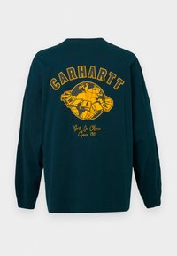 Majica dugih rukava tamno teal boje od pamuka sa žutim grafičkim otiskom globusa i natpisom "CARHARTT" na leđima. Mekana tekstura i opušteni kroj.