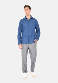 Camicia in denim blu con bottoni e maniche lunghe, abbinata a pantaloni grigi chiari. Sneakers bianche con suola testurizzata completano l'outfit.