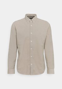 Chemise beige à manches longues boutonnée avec un col pointu, six boutons blancs sur le devant et des poignets boutonnés.