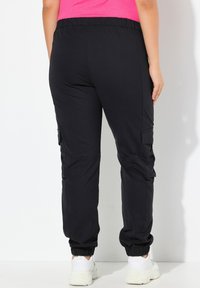 Černé joggingové kalhoty s volným střihem, elastickým pasem, zúženými manžetami a bočními kapsami na cargo. Směs bavlny, jednoduchý design.