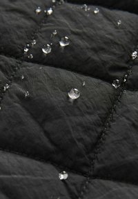 Gouttes d'eau reposant sur un tissu matelassé noir, mettant en avant la texture déperlante du tissu et le motif carré cousu.