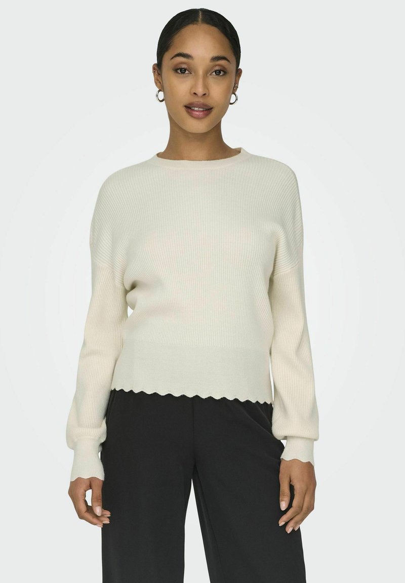 Maglione a coste color crema con scollatura rotonda, maniche lunghe e orlo scalloppato. Abbinato a pantaloni neri a gamba larga, caratterizzati da una texture morbida.