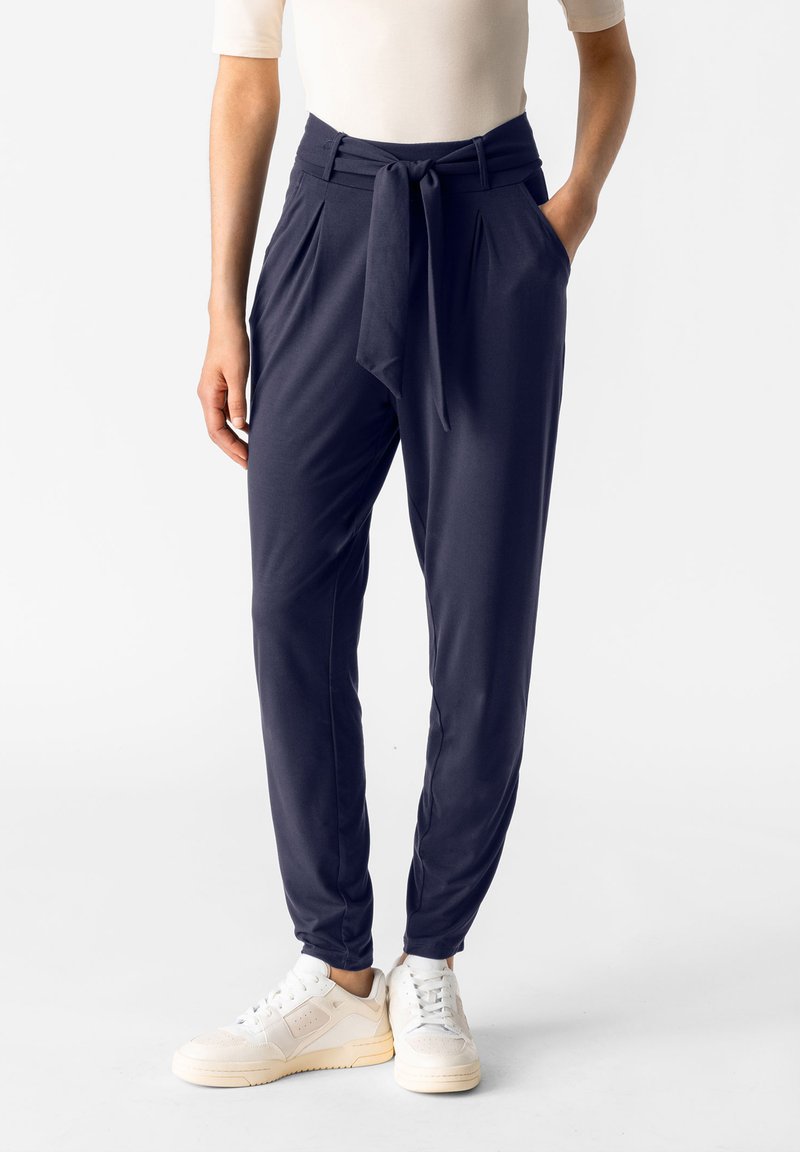 Marinblå byxor med knytdetalj i midjan, elastiska mudd och slät tyg. Matchat med vita sneakers.