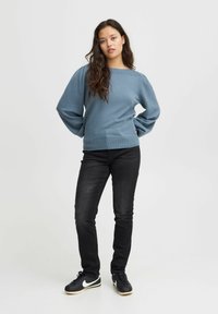 Un pull léger bleu avec des poignets et un ourlet côtelés, associé à un jean noir et des baskets noires avec un logo Nike blanc.