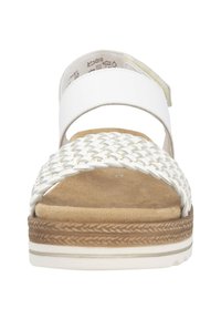 Sandale à brides tressées blanches avec une semelle intérieure souple couleur tan, une semelle flexible et une couture décorative marron clair le long du bord. Talon plat.