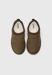 Een paar bruine gevoerde binnenslippers met donkerbruine bies en witte fleece voering, vanboven bekeken op een effen witte achtergrond.
