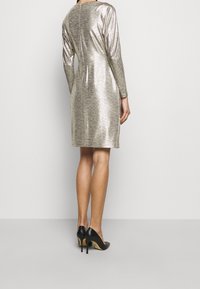 Metallic silver dress with long sleeves and a fitted silhouette, featuring a round neckline and back zipper. Worn with black high-heeled shoes.