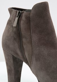 Bottines en velours gris avec un talon haut, dotées d'une fermeture éclair sur le côté et d'une texture lisse. Le design est élégant avec une ouverture effilée.