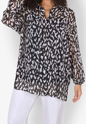 Schwarz-weiße, transparente Leopardenbluse mit langen Ärmeln und Knöpfen, getragen mit weißen Hosen.