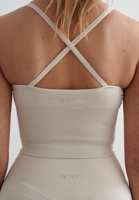 Beige geribbelde sportcrop top met kruislings straps op de rug; heeft een subtiel logo en een soepele, stretchstof.