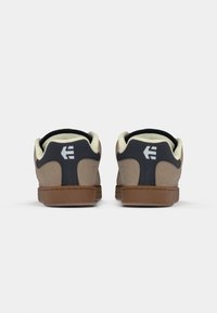 Brown and navy sneakers with a suede upper, padded collar, and rubber sole. Features a white logo on the heel and contrasting color paneling.