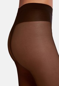 Gennemsigtige brune strømpebukser med en bred mørk taljebånd, glat tekstur og sømløst design, der fremhæver en tæt pasform og en subtil glans.