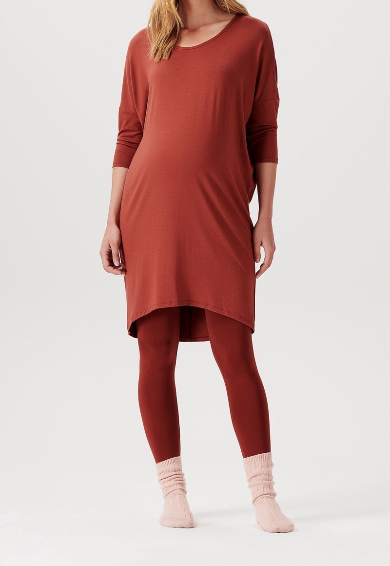 Braunes Umstandskleid mit Dreiviertelärmeln, seitlichen Schlitzen und einem abgerundeten Saum, kombiniert mit passender brauner Leggings und rosa gerippten Socken.